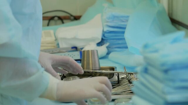 Surgical instrument preparation sequence showing gloved hands placing stainless basin over tray of arranged forceps clamps and scissors on sterile blue drape at midpoint of operation