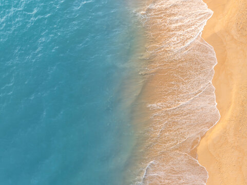 Aerial view of ocean waves gently touching sandy beach shoreline creating a calm coastal pattern. Perfect natural background for tourism promotions, summer visuals, and relaxation themes.