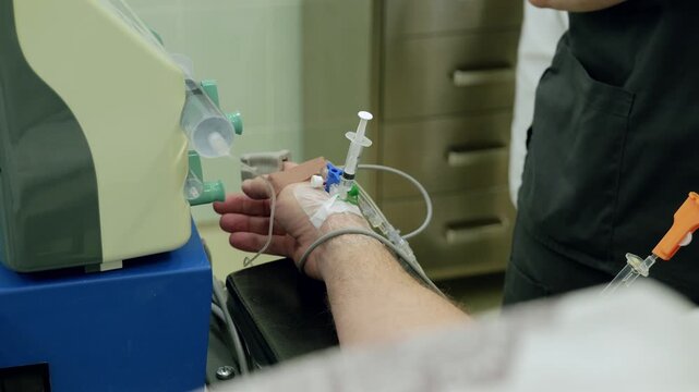 Patient forearm with secured intravenous cannula on padded armrest while clinician adjusts infusion tubing during medication therapy in clean clinical treatment setting