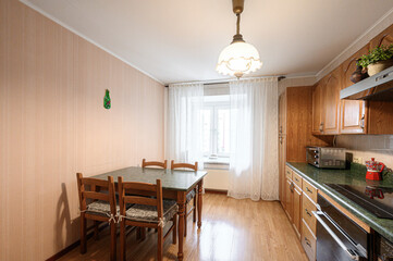 Fototapeta premium kitchen features wooden cabinets with arched doors, a green speckled countertop, a dishwasher, oven, and a dining table with wooden chairs