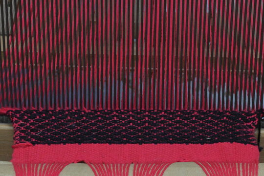  Handmade woven rug with red and black geometric patterns and fringes. Traditional Balkan folk textile art and rustic home decoration.