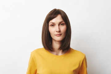 Fototapeta premium Brunette in a yellow shirt stands in a studio, closeup portrait with calm expression and soft lighting against a minimal background, with a clean, modern vibe.