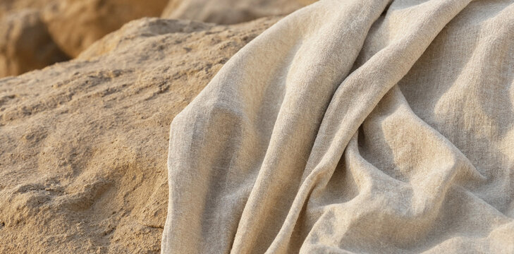 Soft beige fabric draped on rough textured rock with material background minimalist backdrop contrast interior homespun structure composition close-up