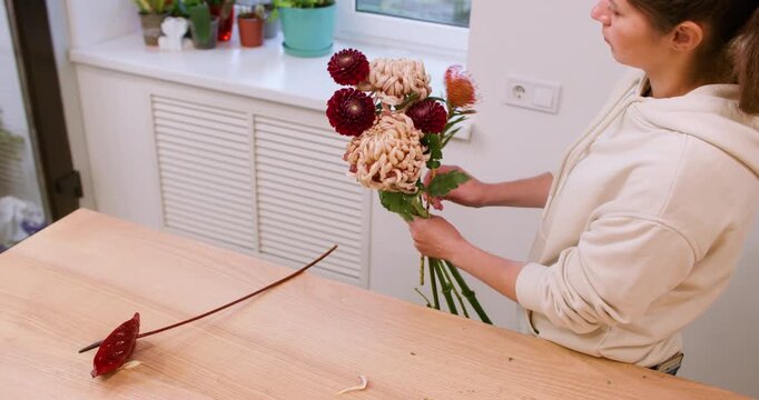 Flower composition. Seasonal floristry. Professional female floral designer arranging autumn color chrysanthemum bouquet in workshop.