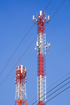 Two telecommunication towers against clear blue sky in vertical frame, transmitting 5G mobile cellular network signals.