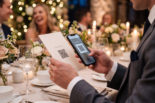 Elegant guest's hands scanning modern QR code on stylish wedding program at reception