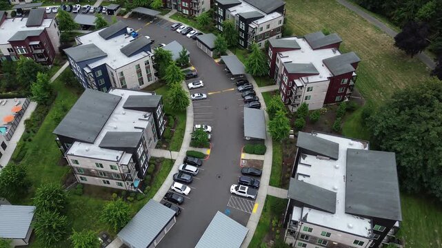 Structured carports line asphalt roadways separating modern apartment blocks in Seattle suburbs. Green lawns border pedestrian sidewalks within multi family housing complexes in Kent, Washington
