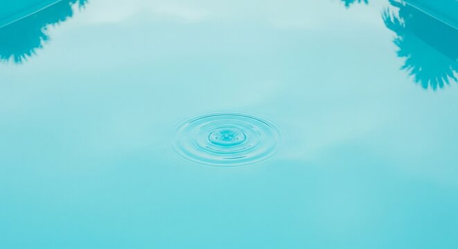 Clear turquoise water in a swimming pool with gentle ripples in the center and reflections of palm tree leaves on the surface.
