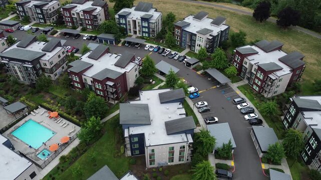 Asphalt drives snake through multi story residential buildings featuring dark shingle roofs suburbs Seattle. Compact vehicle stalls sit adjacent to manicured green spaces in Kent, Washington
