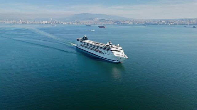 Passenger ship crossing calm sea near urban coastline. Drone view for maritime travel, tourism and cruise transportation