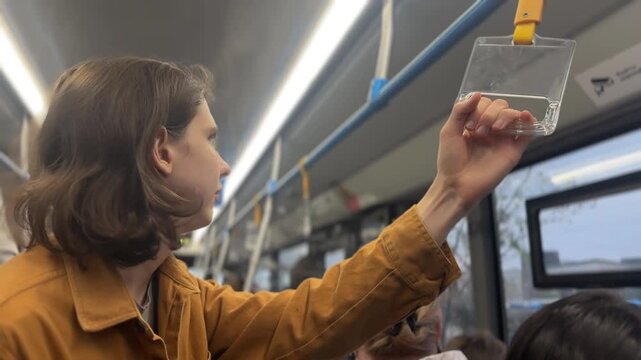 A man stands in the bus with her hand grasping the plastic handrail. The man holds the handrail as the bus moves through the city streets.