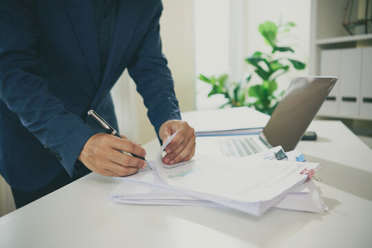 Financial report verification with business professional writing notes on organised documents beside laptop to confirm records improve accuracy support auditing and streamline accounting workflow.