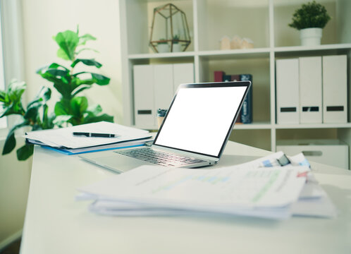 Laptop mockup with blank screen and financial documents on office desk, providing copy space for business analytics accounting software digital reporting and professional presentation.