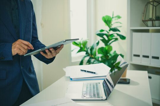 Digital business workflow with professional using tablet beside laptop and documents to review information coordinate tasks improve mobility and support efficient data-driven decisions.