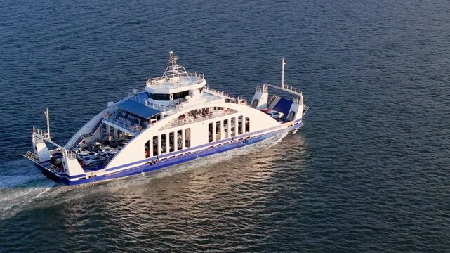 Passenger and vehicle ferry sailing on open water with cars visible on deck. Marine transport for urban traffic connection