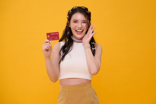 Credit card payment concept with smiling Asian woman presenting a bank card in studio promoting cashless shopping financial freedom online transactions and confident consumer lifestyle.