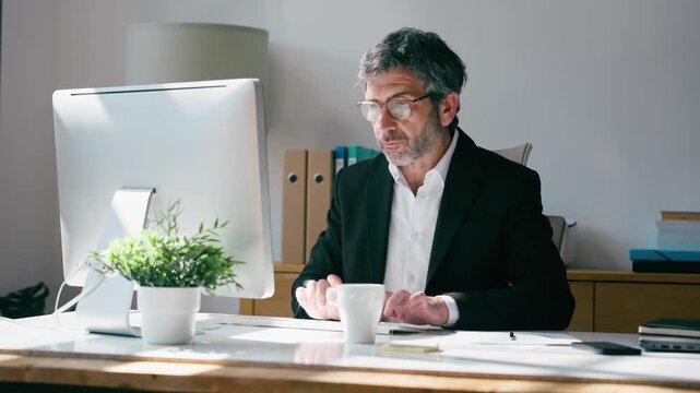Video of elegant businessman drinking coffee while working on a computer in the office