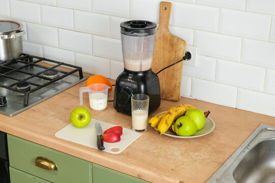 Electric blender on kitchen counter for smoothie making process. Fresh fruits, cutting board, and glass of protein milkshake on table. Healthy lifestyle. Vitamin Boost, Morning Routine and Self Care