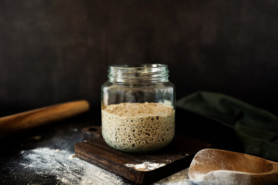 Rustic sourdough rye starter jar with flour on a kitchen counter.