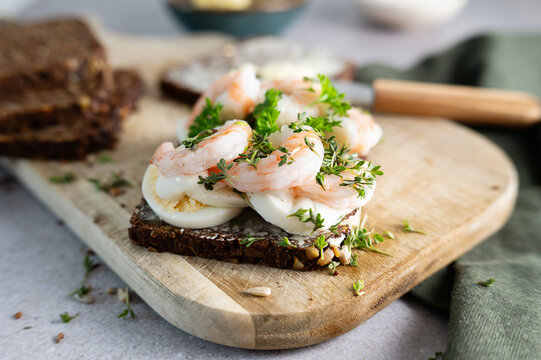 Danish smorrebrod topped with egg, shrimps, and fresh herb.