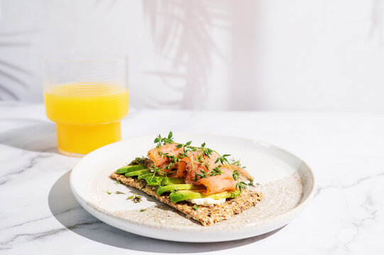 Healthy crispbread breakfast with salmon, avocado, and orange juice.
