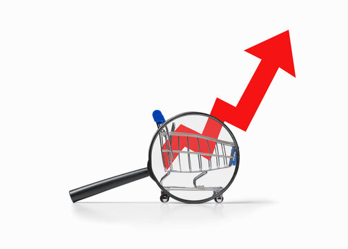Magnifying glass examines shopping cart with rising arrow graphic. Symbolize rising consumer prices. Commerce trend chart.