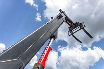 Telehandler telescopic boom raised with forklift pallet forks. Modern construction lifting machinery perspective view against sky background with heavy industrial vehicle details. © NastyaPhoto