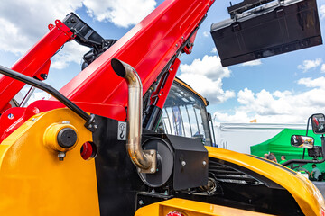 Fototapeta premium Red telehandler exhaust pipe with steel muffler protection. Modern construction machinery yellow chassis section against sky background with hydraulic hoses and industrial transport details.