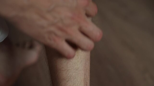 Male person suffering from irritating itch on shin due to mosquito bite, scratching red skin with fingers to find relief from allergic reaction and skin problem, close-up, slow motion.