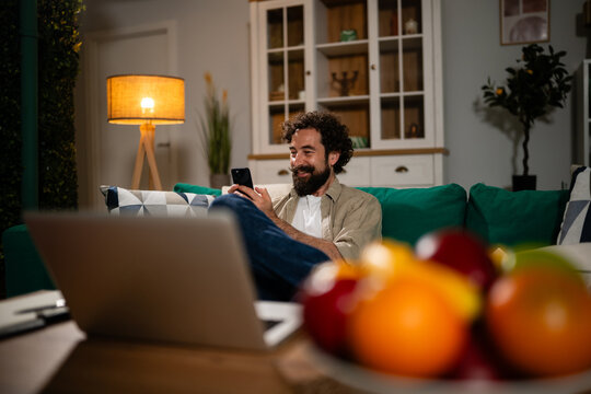 Man relaxing on sofa using smartphone at home