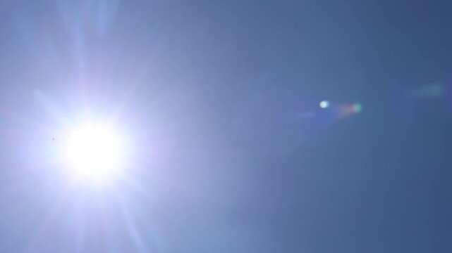Bright sun shining with lens flare in a clear blue sky