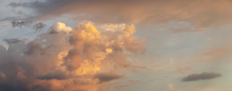Majestic cumulus clouds illuminated by warm sunset light in panoramic sky