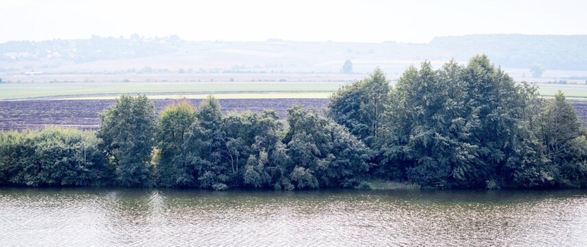 Panoramic landscape with river trees and rural fields on foggy horizon