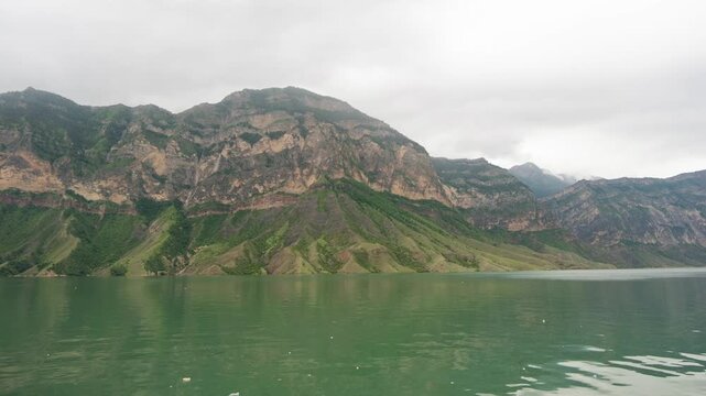 Rain clouds fill the sky over a large mountain lake that is bordered by tall mountains. 