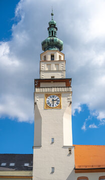 The tower of the town hall stands tall in Boskovice. The clock shows the time while clouds drift by in the sky. The building displays its unique architecture against the blue background.