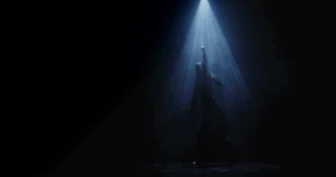 Silhouette of a female dancer performing under a single dramatic overhead spotlight on a dark stage. Concept of dance, performance, nightlife and art, fitness, fashion and entertainment advertising.
