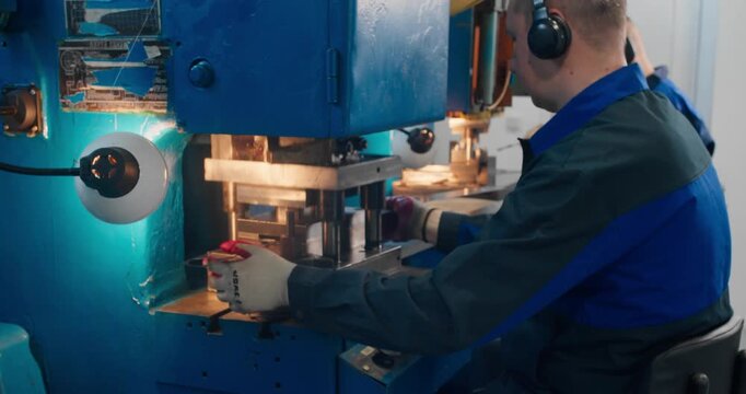 Industrial employees following workplace safety procedures during metal stamping operations in a manufacturing facility