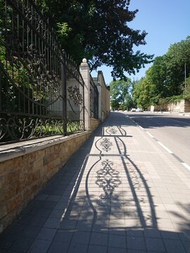 Decorative fence casting shadows on pavement in sunny urban setting  