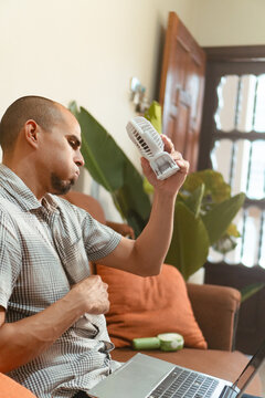 Man cooling himself with portable hand fan at home