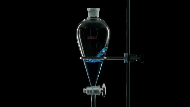 Close-up of blue transparent fluid is injected into a separatory funnel, producing splashes within the liquid over dark background