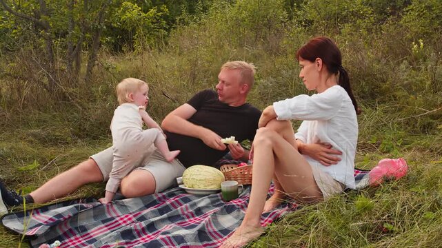 Outdoor family picnic with parents and baby eating together on blanket in field