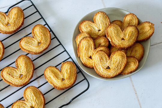 Palmier cookies on a black cooling rack with a plate of cookies on a white ceramic plate 