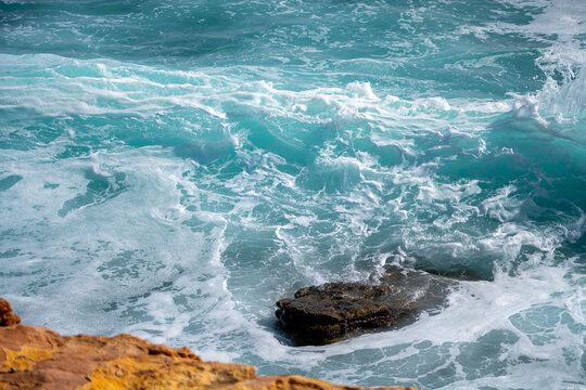 Waves roll heavily against rocks at the shore. The ocean displays high energy as water splashes and foams. The scene captures the power of nature during a stormy day.