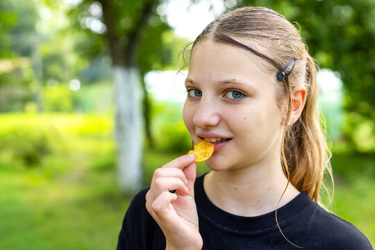Young Girl Eating a Potato Chip Outdoors. Young girl in a black shirt eating a potato chip in a sunny green park.