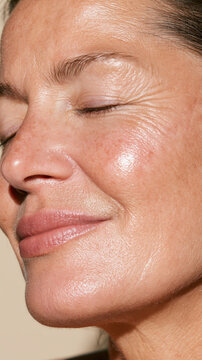 Close up of a smiling woman's face, her eyes closed in relaxation, with natural skin texture, visible freckles, and fine wrinkles celebrating beauty and authenticity