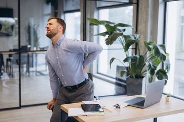 Businessman suffering from lower back pain in the office, indicating poor posture or work related...