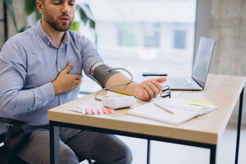 Obraz premium Businessman checking blood pressure facing sudden chest pain at work, suffering from heart attack or hypertension