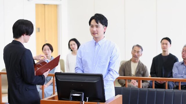 法廷で証言を行う若い男性と裁判を見守る傍聴人