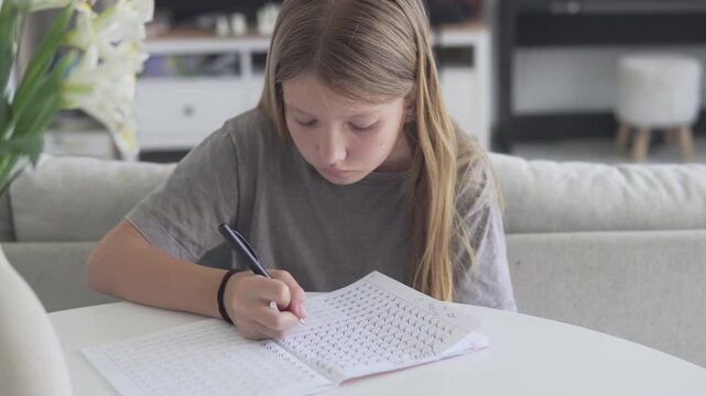 Schoolgirl practicing handwriting and completing writing exercises in a workbook while studying at home