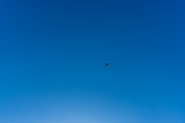 Fototapeta premium Airplane flying across clear blue sky with expansive copy space and minimalist composition highlighting travel, freedom, and aviation concept